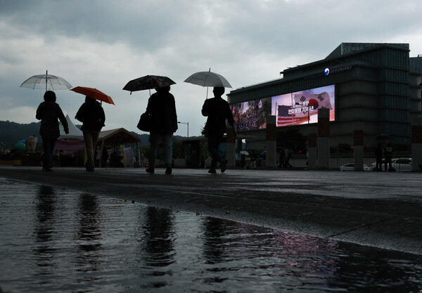 하늘에 드리운 먹구름과 함께 비가 내린 18일 오후 서울 세종대로 광화문광장에서 관광객과 시민들이 우산을 쓴 채 이동하고 있다(사진=연합뉴스)